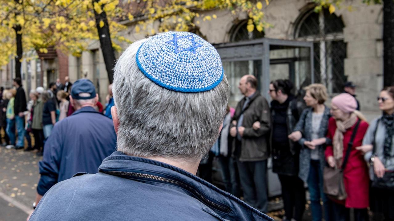Ein Mann mit Kippa steht vor der Neuen Synagoge Berlin vor einer Menschenkette.