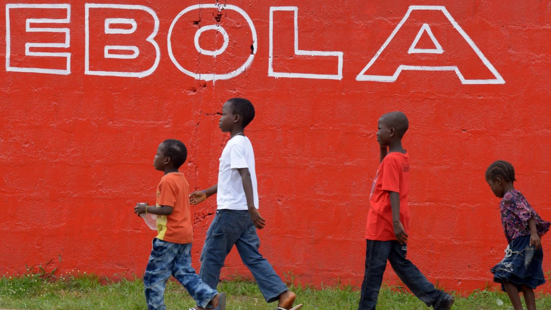 Vier Kinder im Schulkindalter laufen vor einer knallroten Mauer mit der weißen Aufschrift "Ebola".