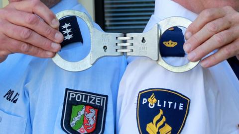 Deutsche und niederländische Polizisten posieren in einer gestellten Situation am Mittwoch (25.05.2011) in Mönchengladbach gemeinsam mit Handschellen. Staatsanwaltschaft und Polizei aus der deutsch-niederländischen Grenzregion beraten auf einer Tagung die Verbesserung in der Zusammenarbeit. Foto: Roland Weihrauch dpa/lnw | Verwendung weltweit