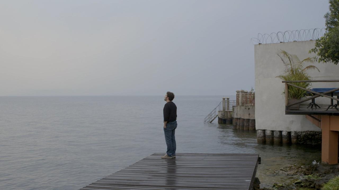 Ein Mann steht vor einem großen Gewässer auf einem Kai.