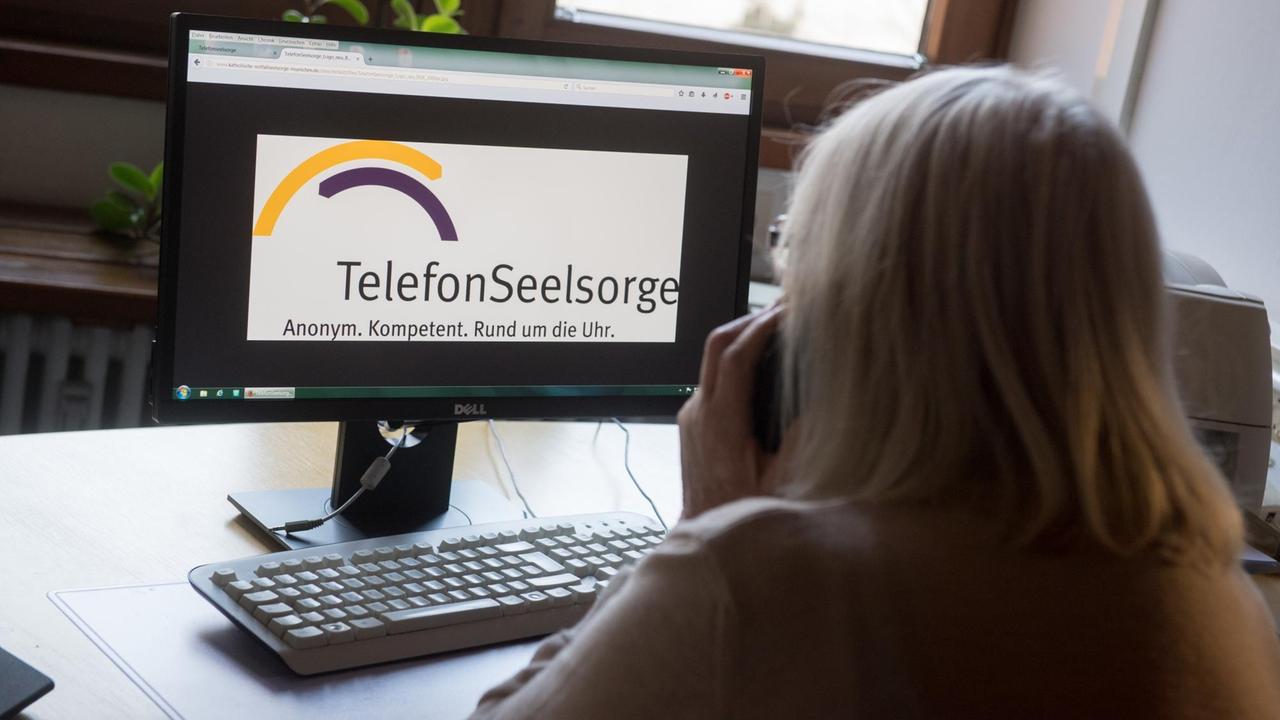 Eine ehrenamtliche Mitarbeiterin der evangelischen Telefonseelsorge München hält einen Telefonhörer an einem Arbeitsplatz für Seelsorger während die Homepage der Telefonseelsorge auf einem Monitor zu sehen ist.