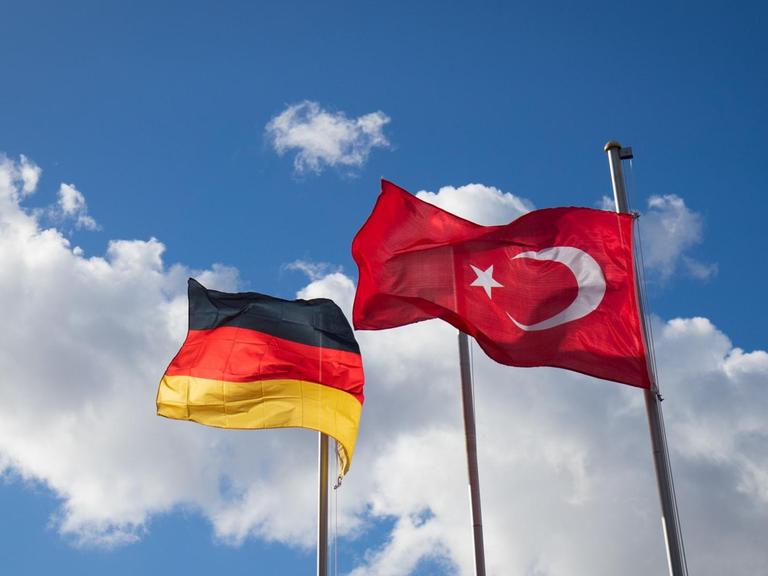 Die deutsche und die türkische Flagge sind an Fahnenmasten zu sehen. Im Hintergrund ziehen Wolken auf.