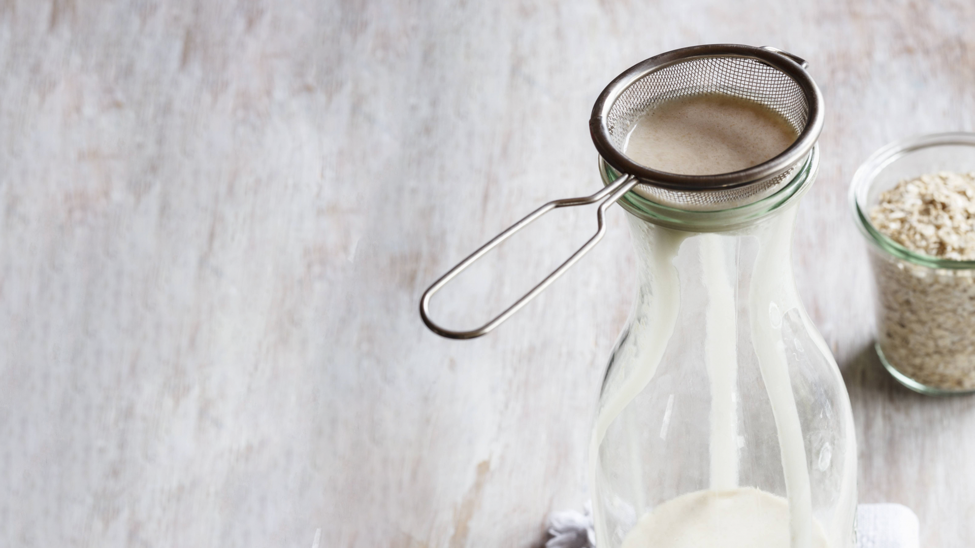 Mit Haferflocken, einer Flasche, einem Sieb und Wasser wird Hafermilch gemacht.