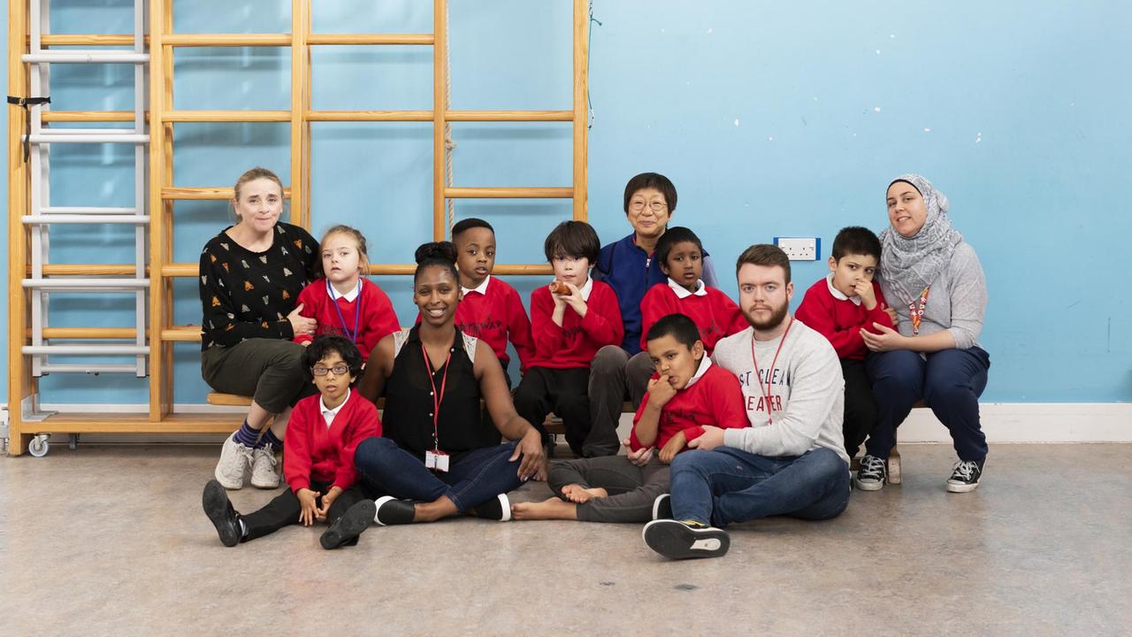 Eine Schulklasse mit roten Pullovern sitzt mit ihren Lehrern vor einer hellblauen Wand
