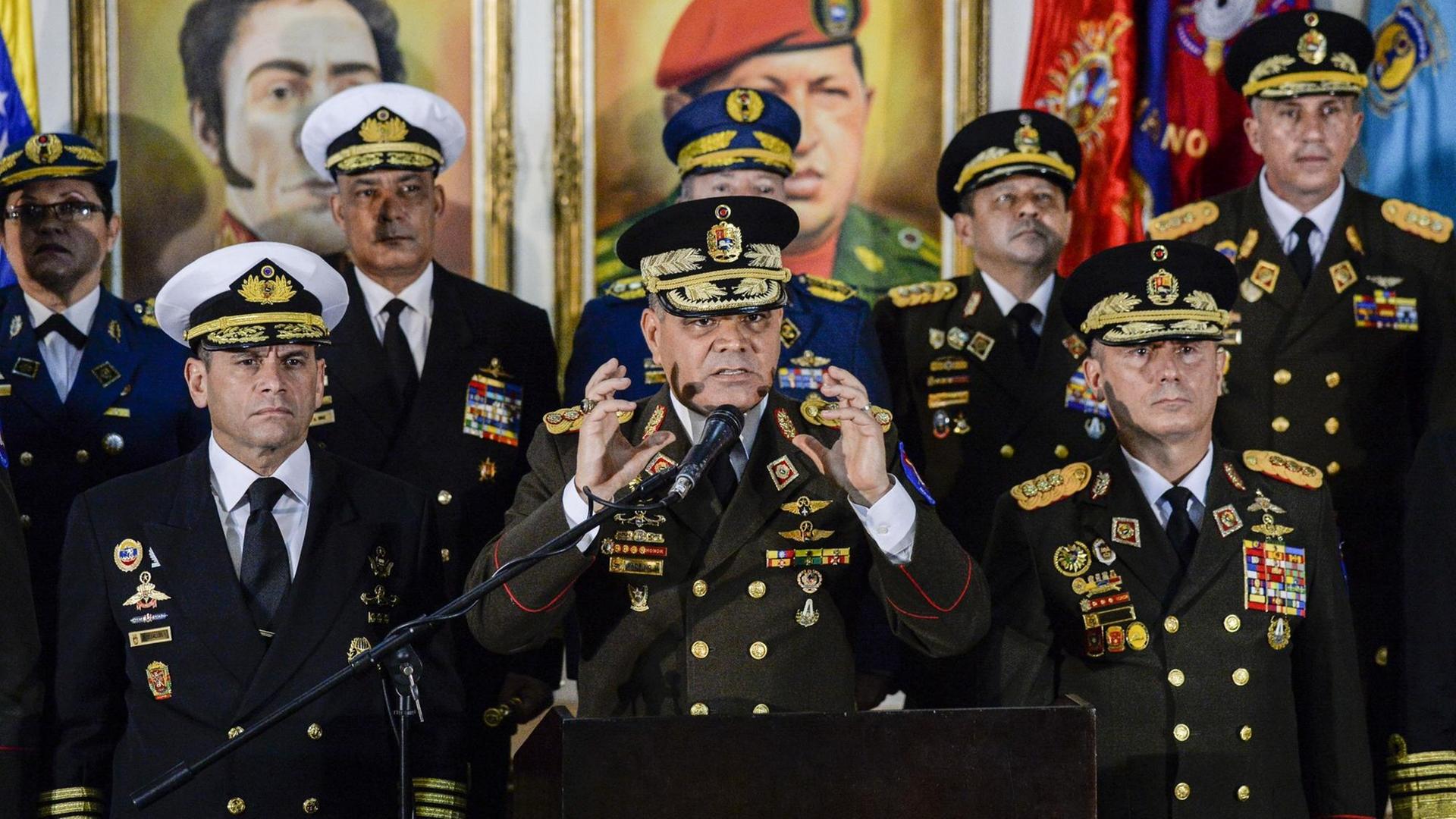 Das Bild zeigt Venezuelas Verteidigungsminister Vladimir Padrino gestikulierend während einer Erklärung hinter einem Mikrofon. Er trägt eine Uniform und ist umringt vonanderen Militärs.
