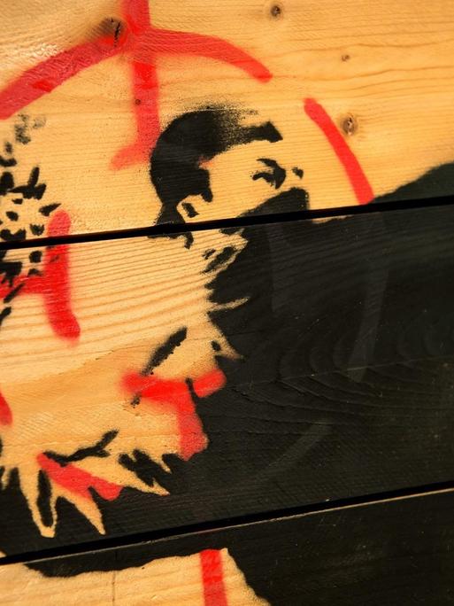 Graffii von Banksy zeigt einen Vermummten, der ausholt um einen Strauß Blumen zu werfen.