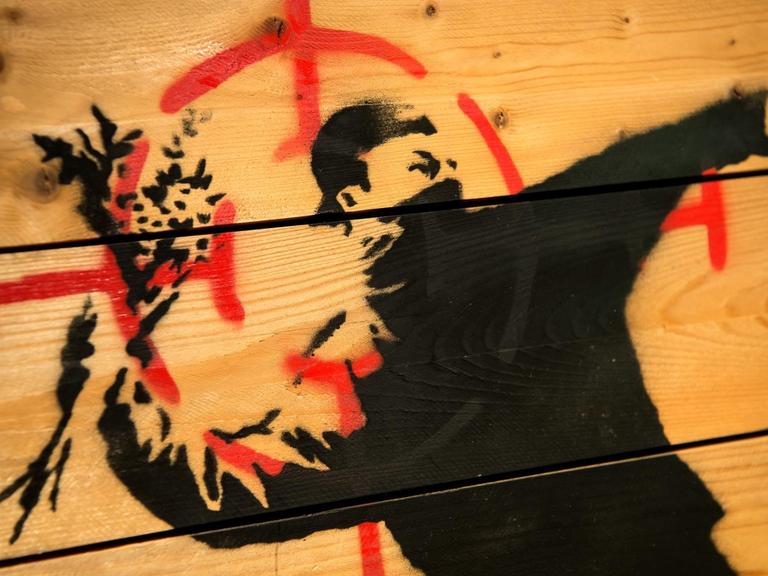 Graffii von Banksy zeigt einen Vermummten, der ausholt um einen Strauß Blumen zu werfen.