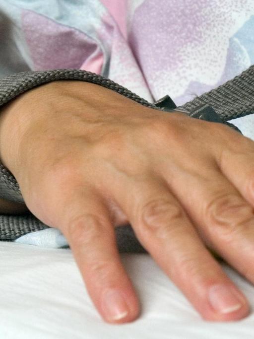 Das Foto zeigt eine mit einem Textilband festgebundene Hand eines Patienten.