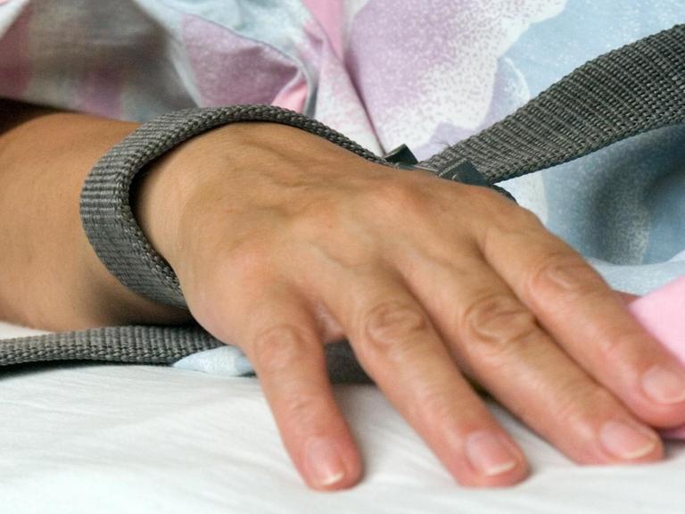 Das Foto zeigt eine mit einem Textilband festgebundene Hand eines Patienten.