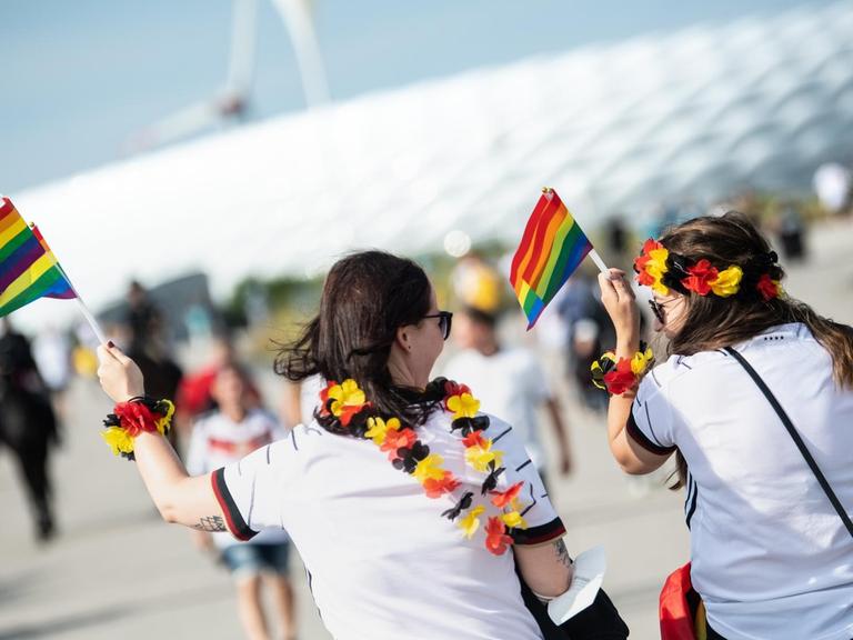 Zwei weibliche Fußballfans kommen mit Regenbogenfahnen zum Stadion in München.