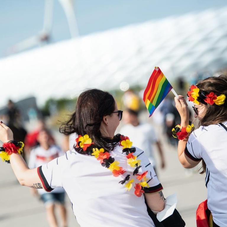 Zwei weibliche Fußballfans kommen mit Regenbogenfahnen zum Stadion in München.