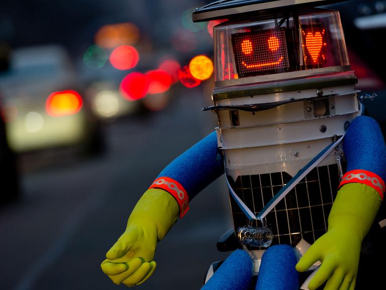 Der trampende Roboter hitchBOT sitzt am 12.02.2015 in München am Straßenrand und lächelt in die Kamera.