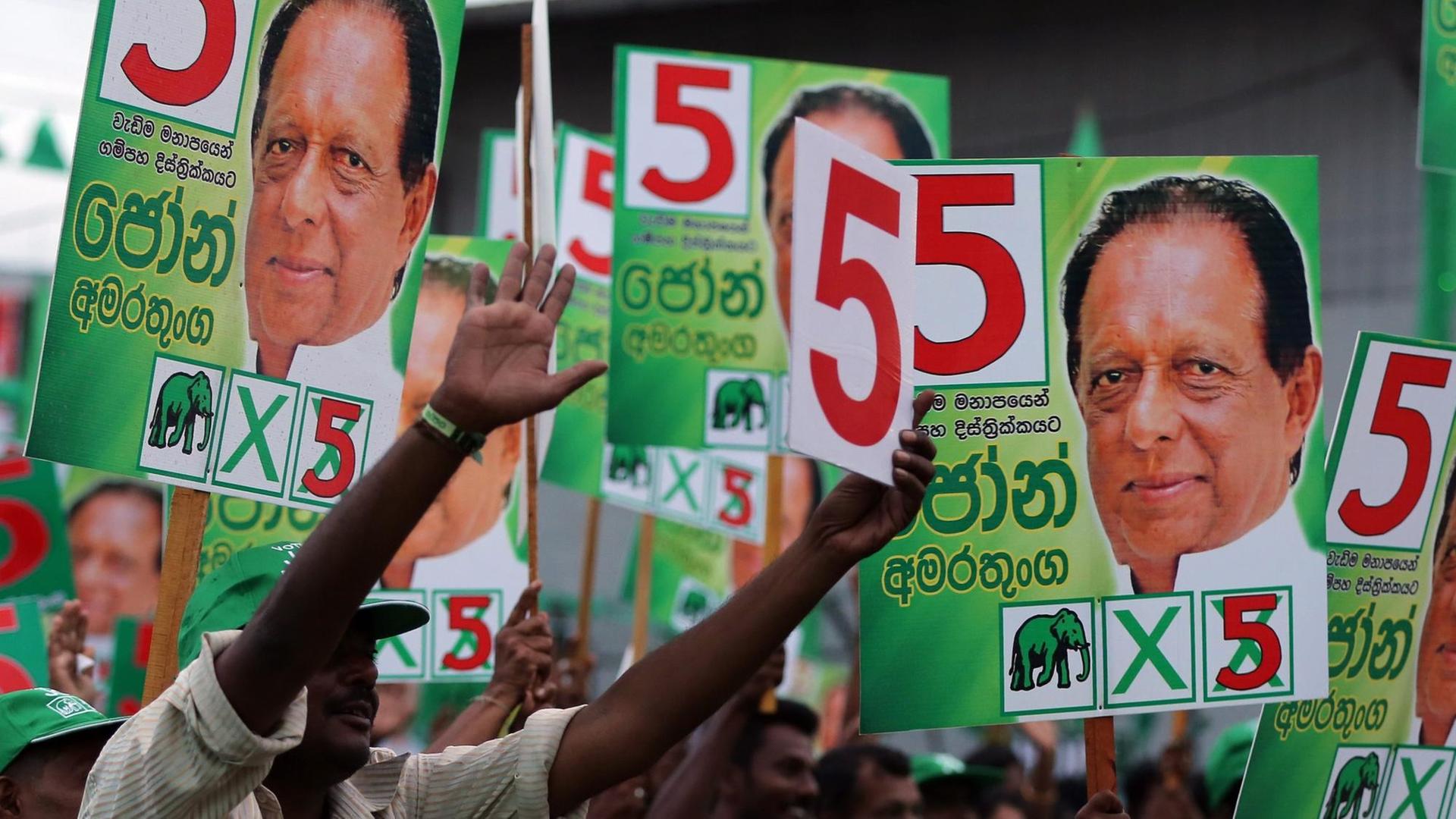 Menschen in Sri Lanka halten Wahlplakate mit dem Konterfei von Maithripala Sirisena in die Höhe.