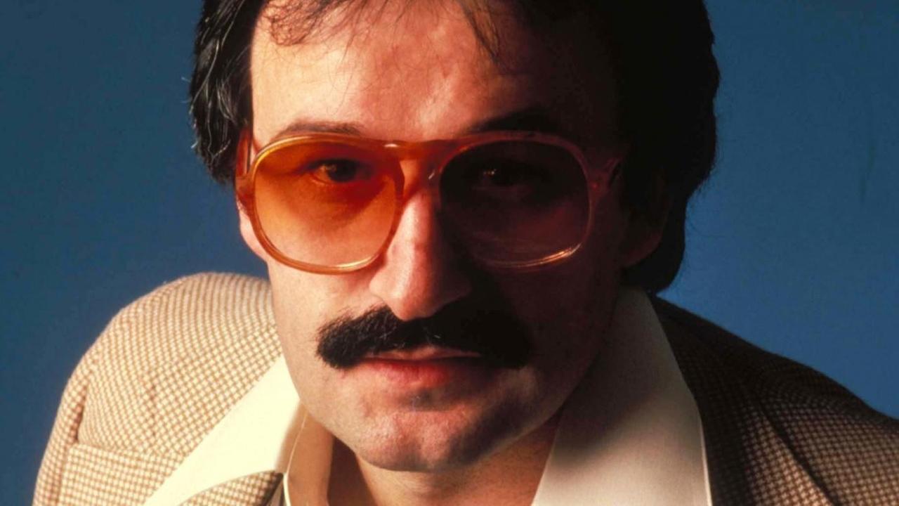 Porträt der Disco-Legende Giorgio Moroder in den 1970er-Jahren mit rot getönter Brille und breitem Hemdkragen.