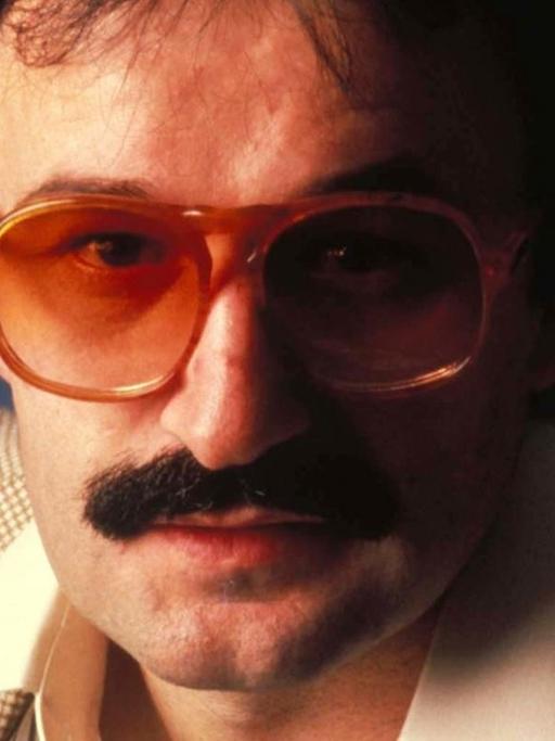 Porträt der Disco Legende Giorgio Moroder in den 1970er Jahren mit rot getönter Brille und breiten Hemdkragen.