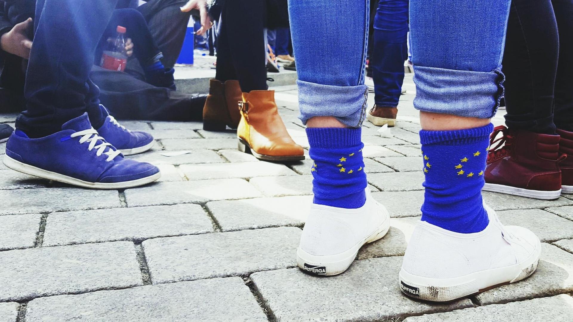 Die Füße mehrerer Demonstranten, von denen einer Socken mit dem Motiv der Flagge der Europäischen Union trägt.