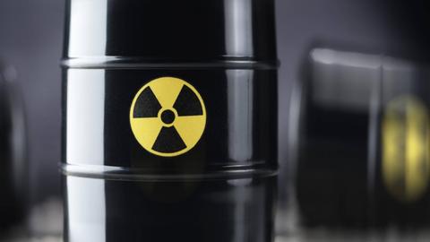 Drei schwarze Atommüll-Fässer, wobei eines im Vordergrund in der Mitte scharf abgebildet ist, im Hintergrund zwei weitere Fässer unscharf.