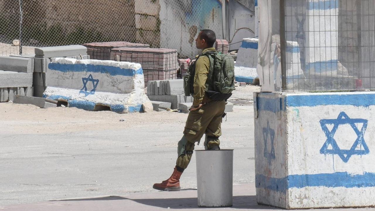 Israelische Kontrollstelle in Hebron im Westjordanland/Palästina: Ein Israelischer Soldat in Uniform steht vor einem Wachhäuschen, das mit einer gemalten israelischen Flagge angestrichen ist.