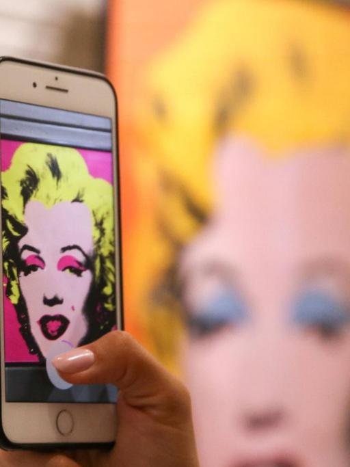 In einer Austellung im Moskauer Granatny Dvor Kultur- und Ausstellungszentrum macht eine Besucherin Aufnahmen eines ausgestellten Kunstwerks von Andy Warhol, das Marilyn Monroe zeigt.