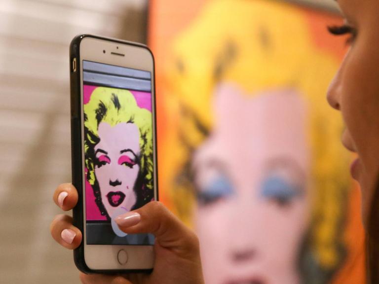 In einer Austellung im Moskauer Granatny Dvor Kultur- und Ausstellungszentrum macht eine Besucherin Aufnahmen eines ausgestellten Kunstwerks von Andy Warhol, das Marilyn Monroe zeigt.