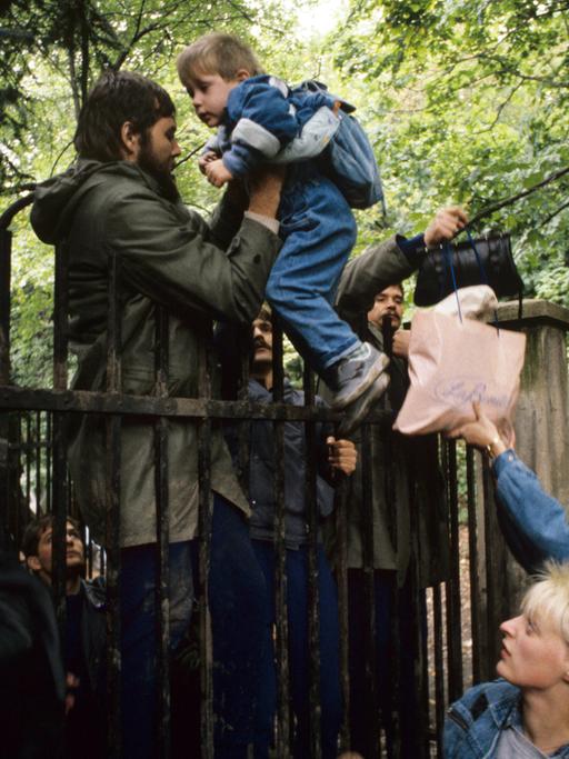 Ausreisewillige DDR-Bürger steigen am 29.9.1989 mit ihren Kindern über den Zaun der bundesdeutschen Botschaft in der tschechoslowakischen Hauptstadt Prag.