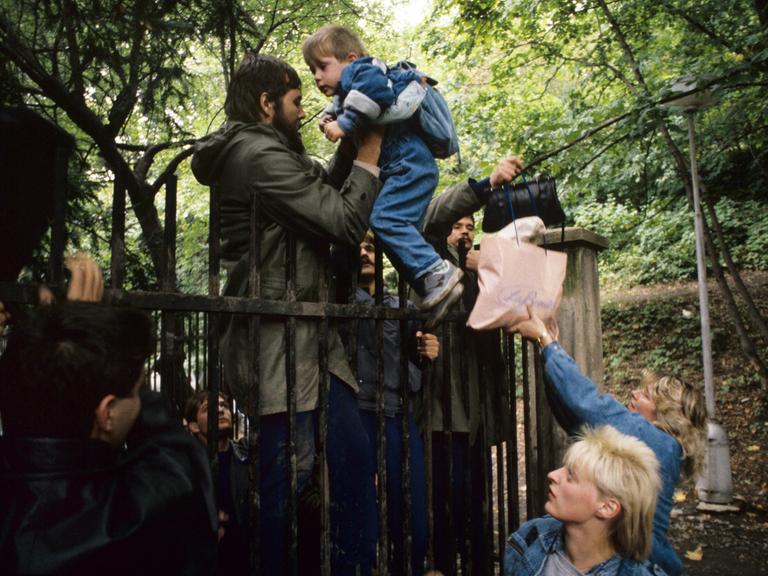 Ausreisewillige DDR-Bürger steigen am 29.9.1989 mit ihren Kindern über den Zaun der bundesdeutschen Botschaft in der tschechoslowakischen Hauptstadt Prag.