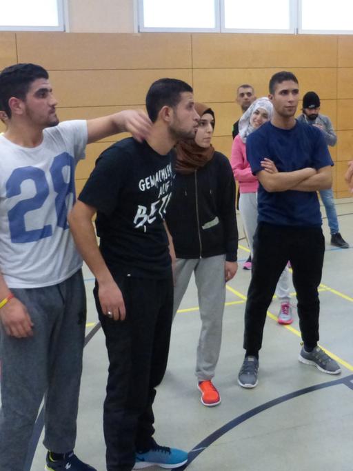 Flüchtlinge stehen in einer Berliner Sporthalle und hören einem Trainer zu.