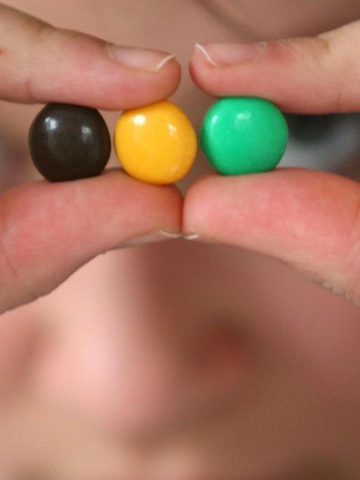 Symbolbild - Ein junges Mädchen hält schwarze, gelbe und grüne "Smarties" als Symbol für eine Jamaika-Koalition in der Hand.