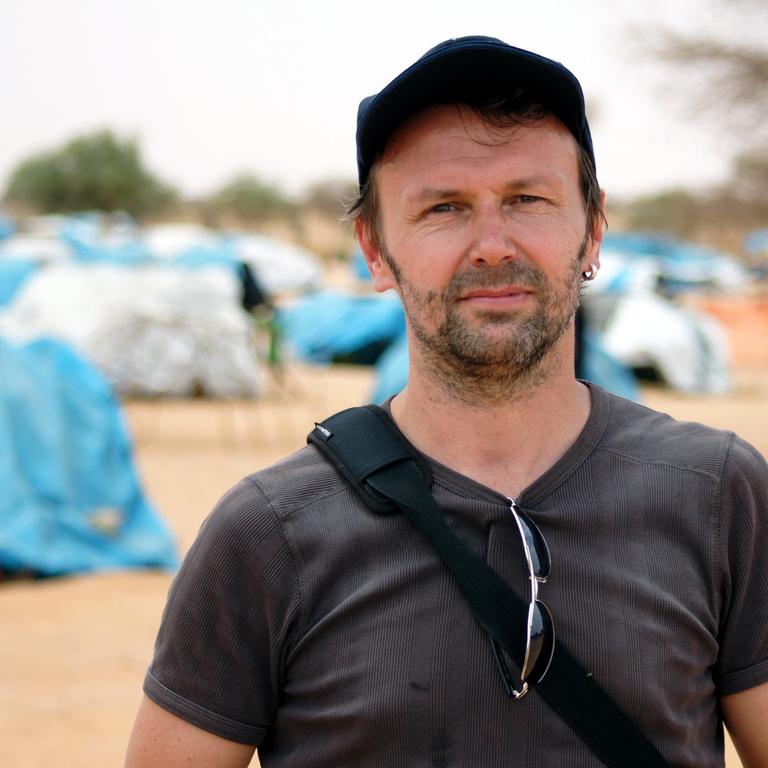 Ralf Südhoff, Chef des Welternährungsprogramms (WFP), steht vor blauen zelten mit Flüchtlingen in der Sahelzone