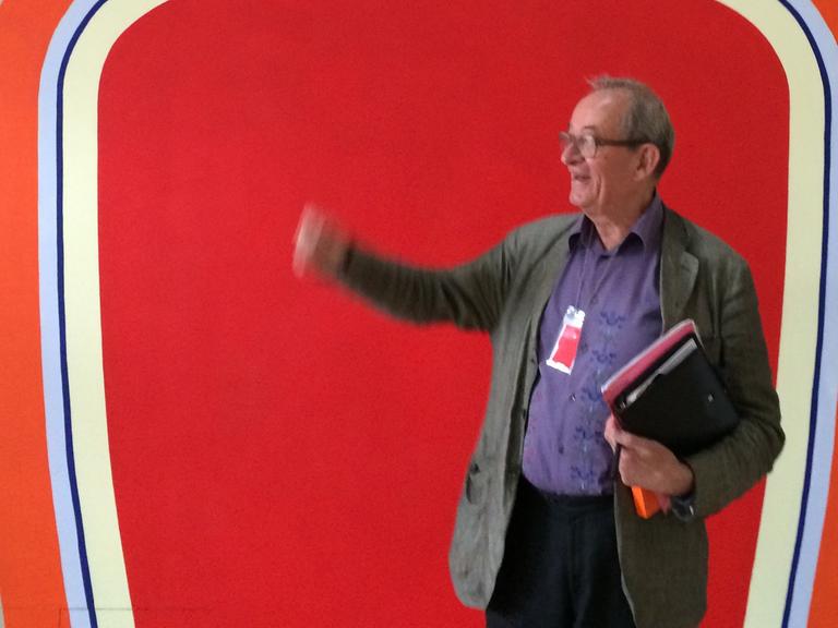 Kasper König gestikuliert vor einem roten Hintergrund