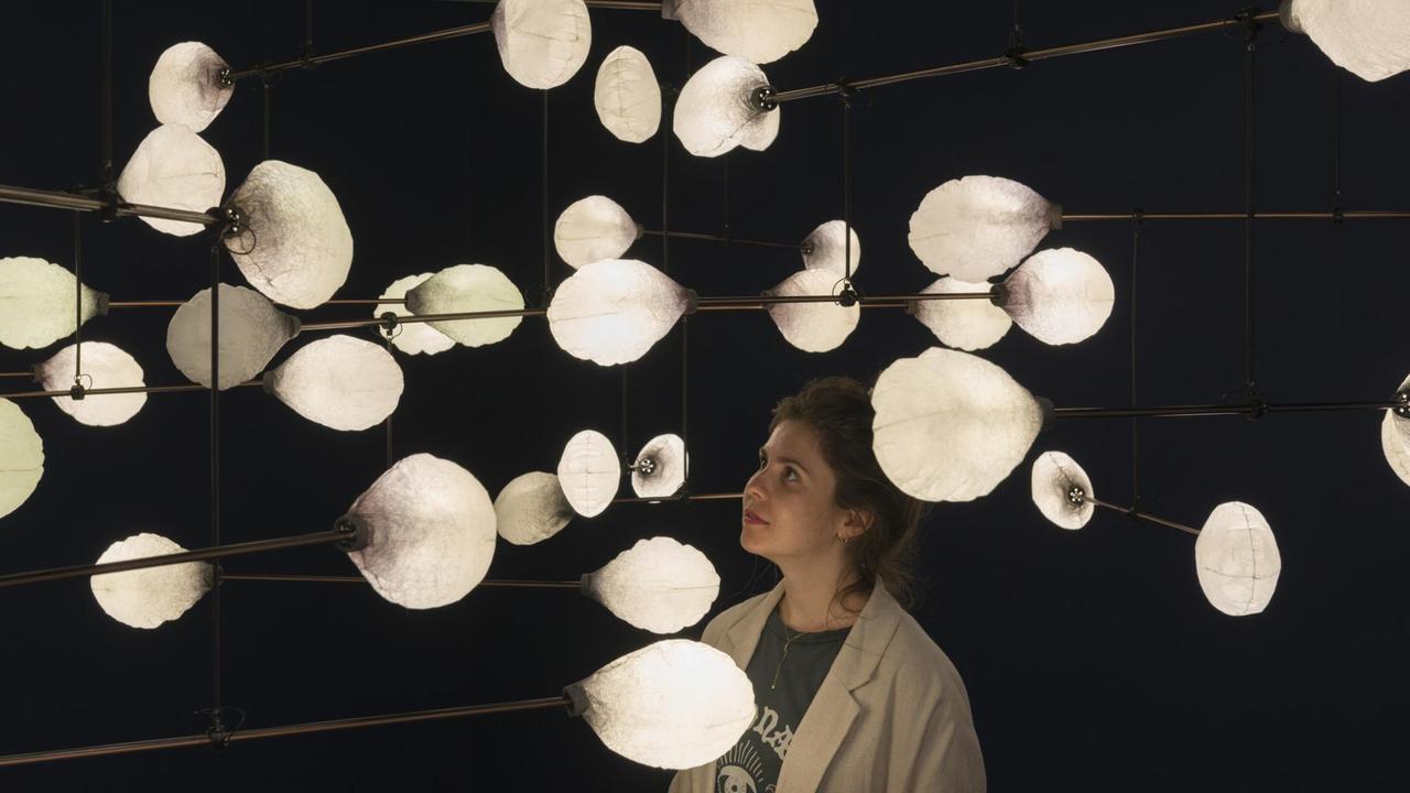 Die Installation "LeveL  the Fragile Balance of Utopia", 2016, von mischer'traxler, bestehend aus weißen, lampionartigen Lichtern. Eine Museumsbesucherin besichtigt die Installation.