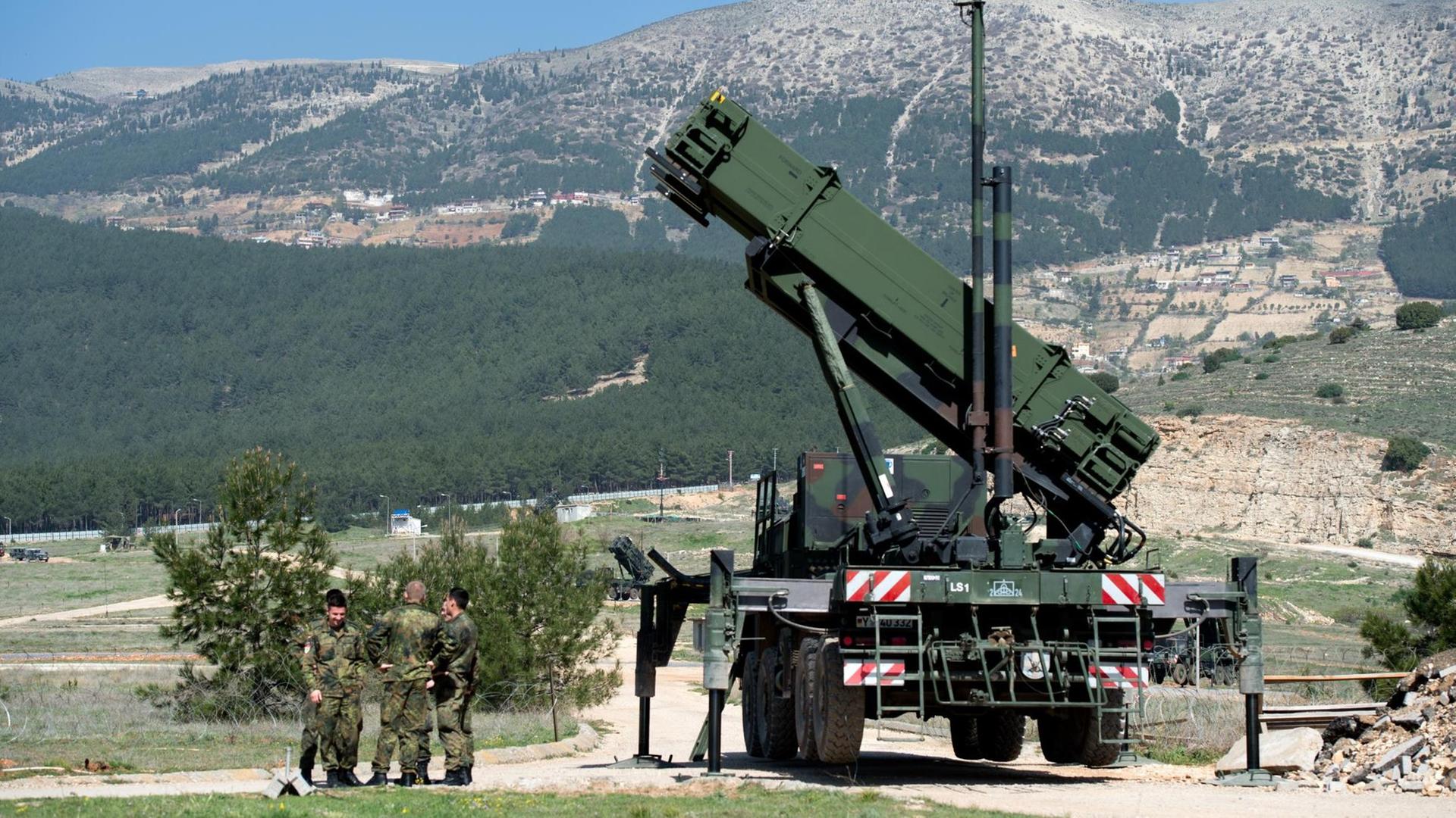 Deutsche Soldaten stehen neben einem "Patriot"-Raketensystem in Kahramanmaras, Türkei. Im Hintergrund sind Berge zu sehen.