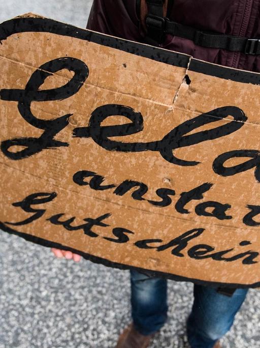 Ein Teilnehmer einer Demonstration für die Rechte von Flüchtlingen zieht am 14.11.2015 in Hamburg durch die Innenstadt und hält ein Plakat mit der Aufschrift "Geld statt Gutscheine" fest.