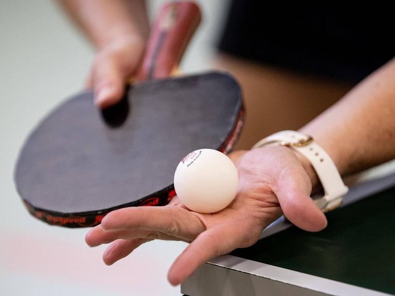 Eine Hand hät einen Tischtennisball direkt vor dem Aufschlag, die andere den Schläger