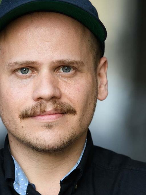 Ein junger Mann mit Basecap steht angelehnt an einer Wand.