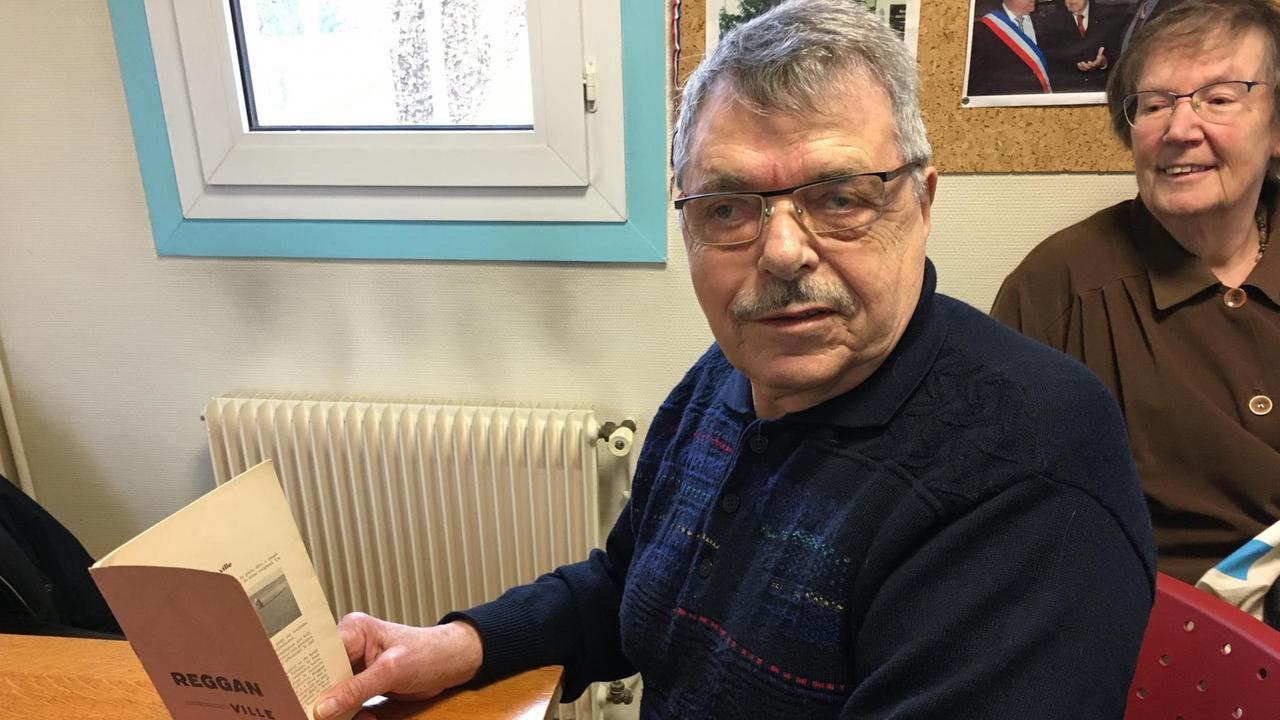 Der Algerien-Veteran Guy Morvan sitzt an einem Tisch und hält ein Buch in der Hand.