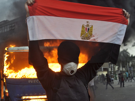 Ein Demonstrant hebt die ägyptische Flagge vor dem Hintergrund brennender Fahrzeuge auf dem Tahrirplatz in Kairo Ein Demonstrant hebt die ägyptische Flagge vor dem Hintergrund brennender Fahrzeuge auf dem Tahrirplatz in Kairo