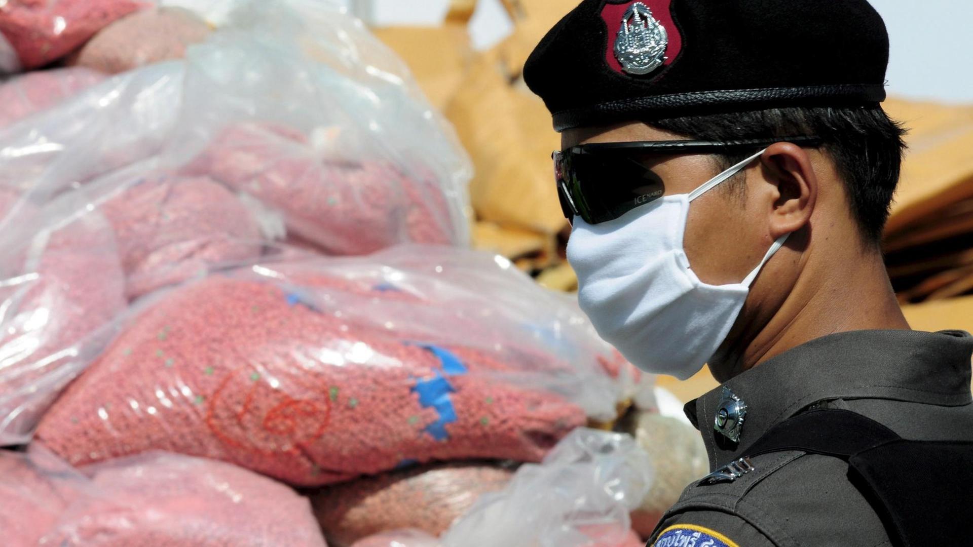 Ein Polizist mit Mundschutz und Sonnenbrille im Profil vor einem Haufen in Plastiktüten voller rosafarbener Pillen, die die Modedroge Yaba enthalten, laut dpa sind es knapp drei Tonnen. Aufgenommen am 26. Juni 2008 in Thailand