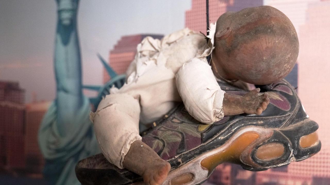 Eine kaputte Puppe liegt auf einem Turnschuh, der im Museum des Meeres von der Decke hängt.