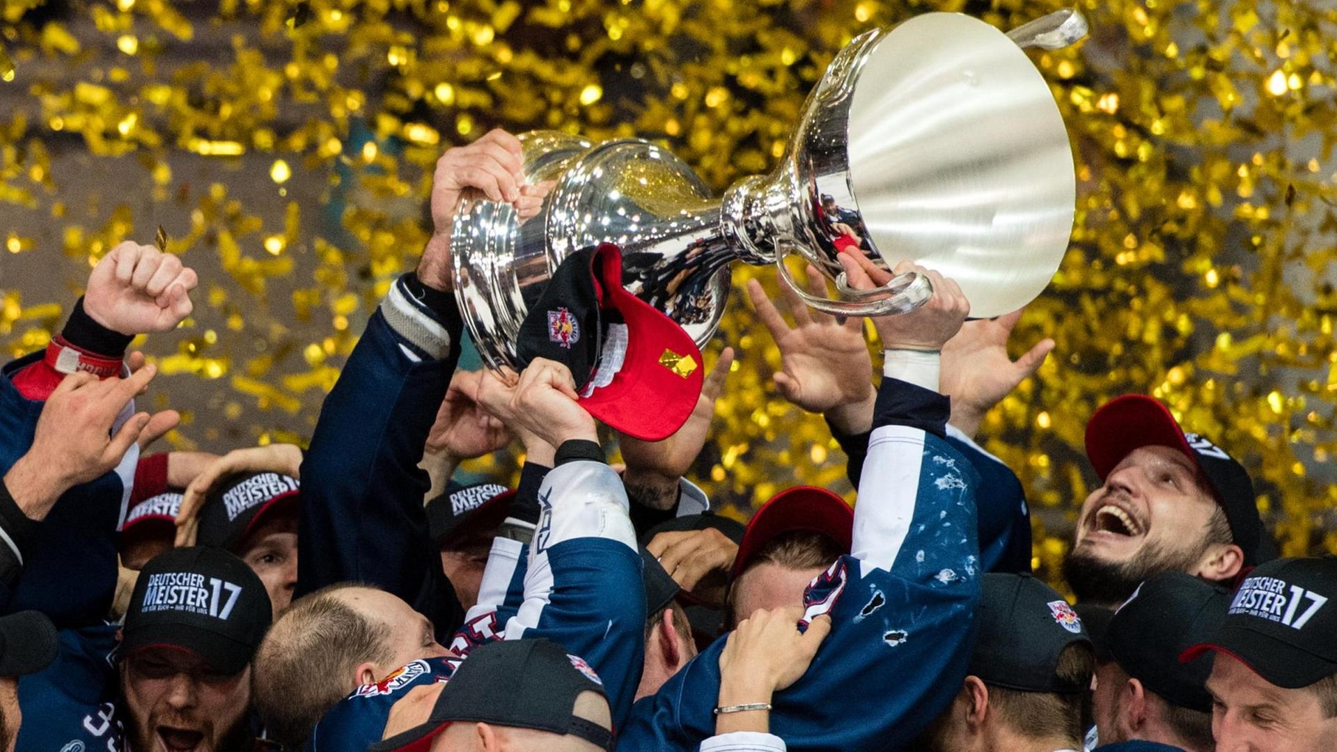 Sie sehen Münchner Eishockey-Spieler, sie halten einen großen Pokal in die Höhe.