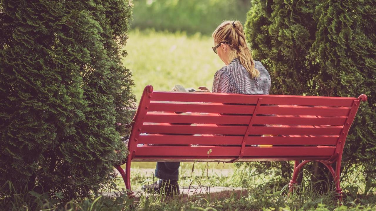Eine Frau sitzt auf einer Parkbank und liest ein Buch.