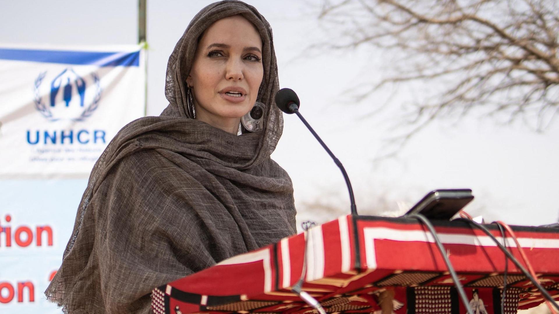 Angelina Jolie seht mit einem Kopftuch bekleidet vor einem Pult mit einem Mikrofon. Angelina Jolie seht mit einem Kopftuch bekleidet vor einem Pult mit einem Mikrofon.
