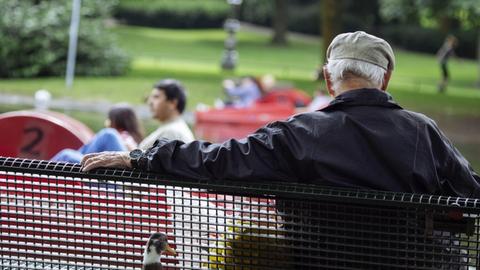 Ein Rentner sitzt auf einer Parkbank.