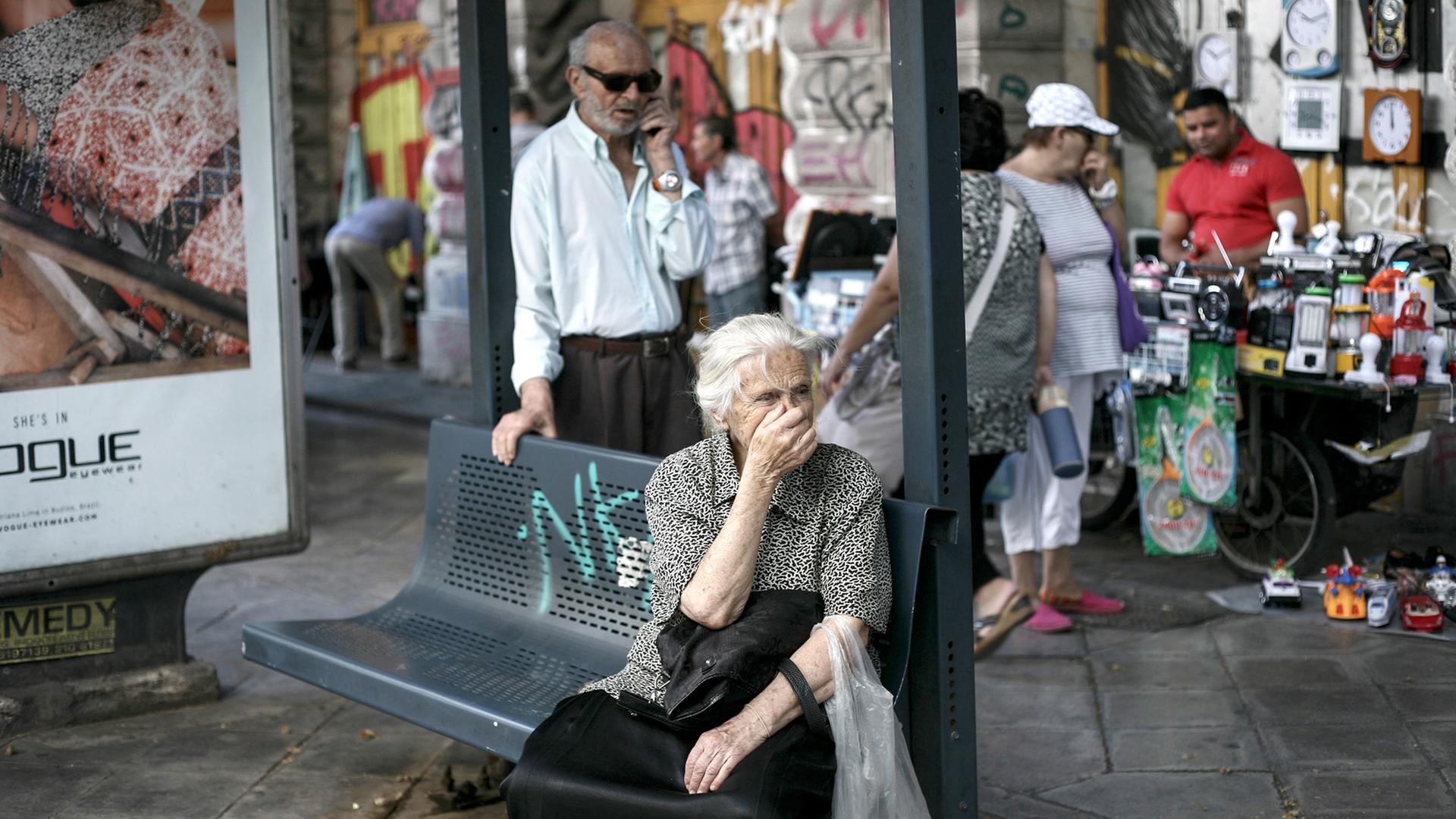 Eine Seniorin wartet an einer Bushaltestelle in Athen.