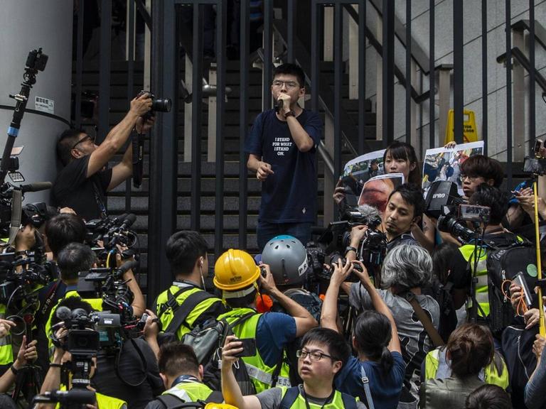 Joshua Wong steht vor den Toren des Hongkonger Polizeipräsidiums. Umringt von Journalisten und Kameras spricht er zu Demonstranten.