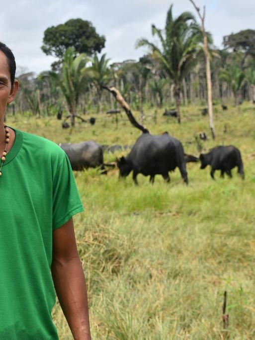 Junger Brasilianer steht mit mürrischem Gesicht vor einer Weide mit Büffeln