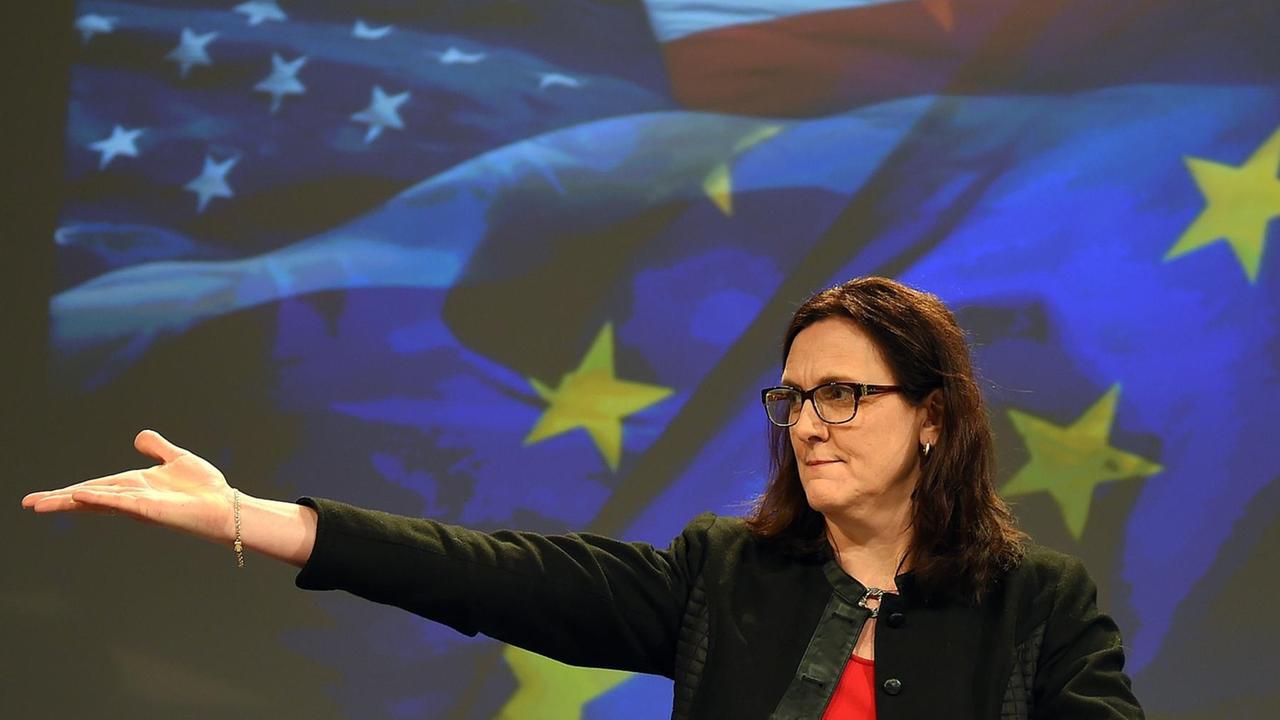 Malmström steht vor einer Videowand mit den Fahnen Europas udn der EU. Sie weist mit einer ausladenden Bewegung der rechten Hand zur Seite.