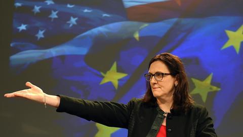 Malmström steht vor einer Videowand mit den Fahnen Europas udn der EU. Sie weist mit einer ausladenden Bewegung der rechten Hand zur Seite.