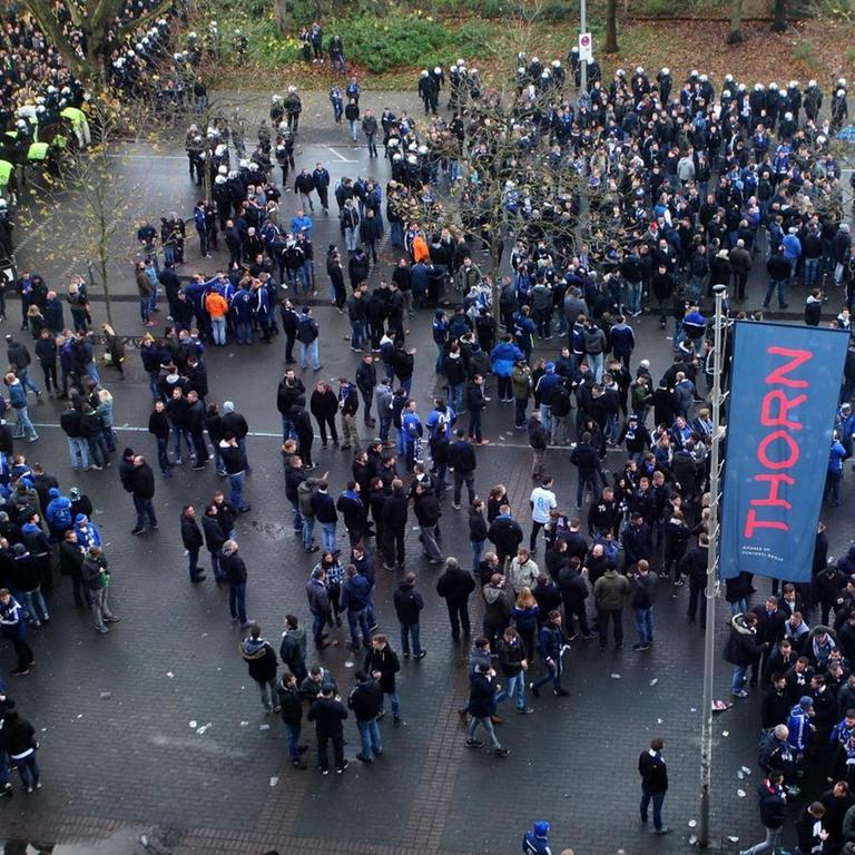 Schalkefans stehen durch Polizisten getrennt von den Dortmund-Fans vor dem Stadion. Luftaufnahme