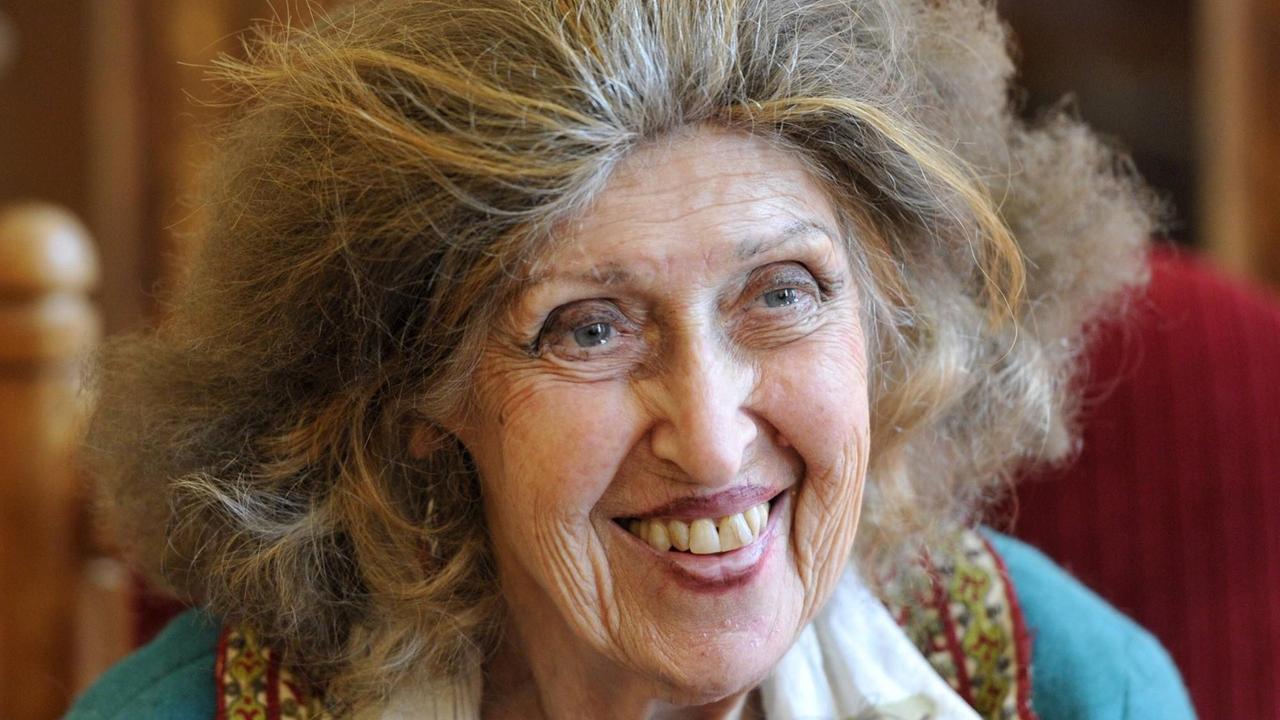 Eine ältere Frau mit langen Haaren lacht jemanden an.